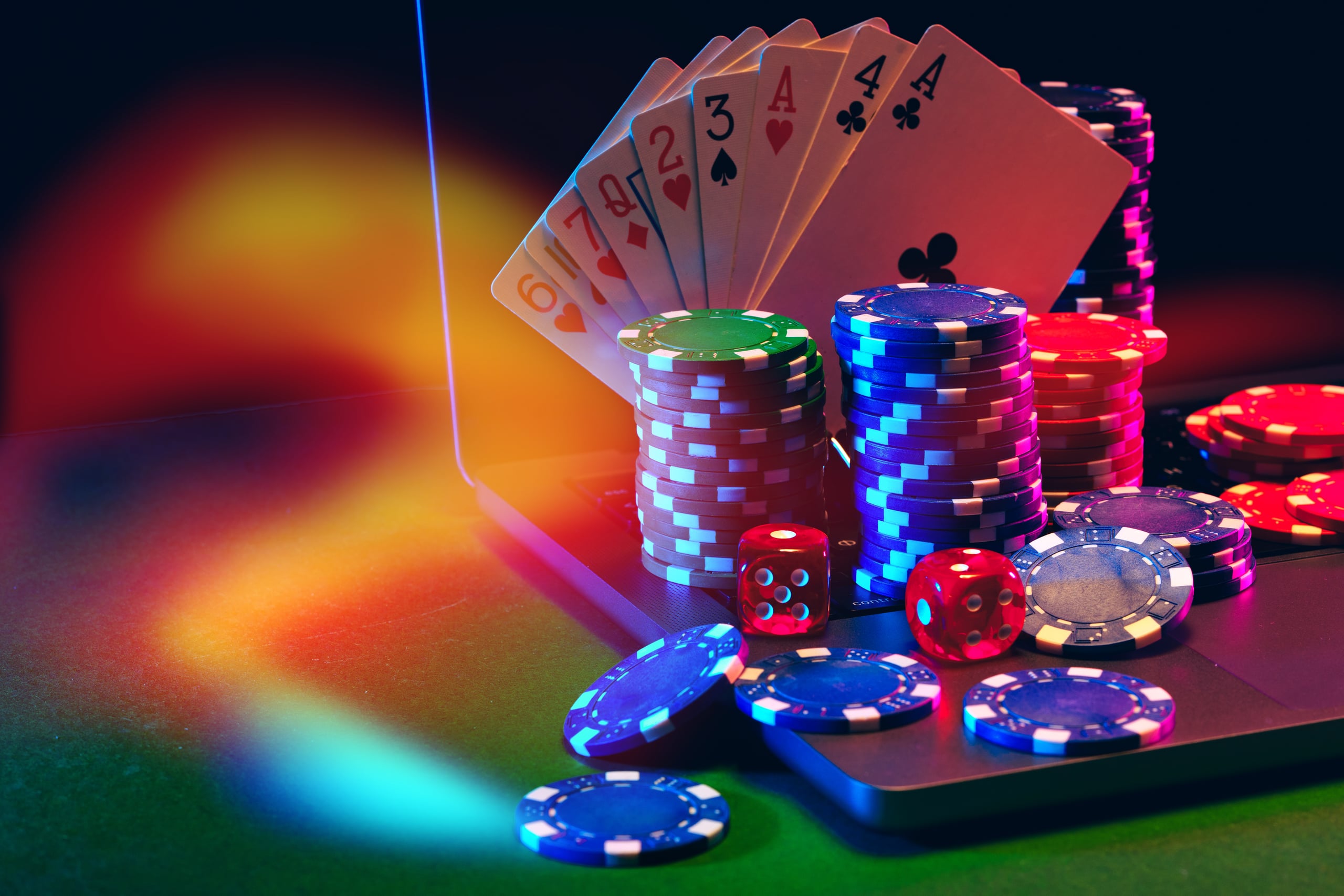 Cartas de póquer en abanico, fichas de colores y dados rojos sobre el teclado de un portátil